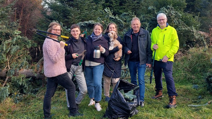Gruppe von Menschen, die im Freien posieren, mit Bäumen und Bergen im Hintergrund.