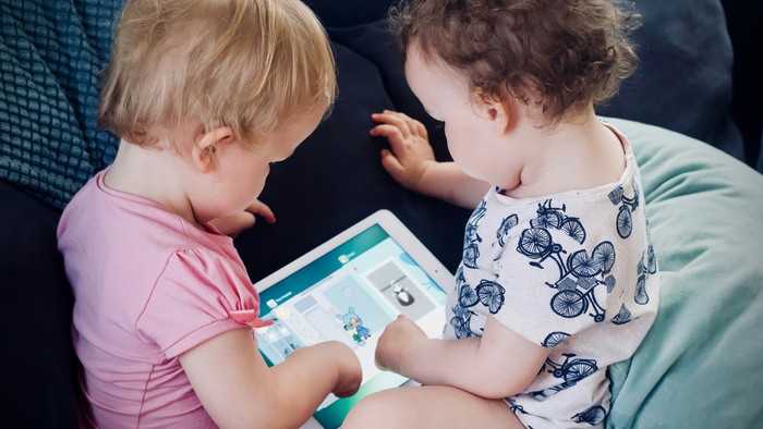 Zwei kleine Kinder sitzen gemeinsam auf einem Sofa und schauen auf ein Tablet.