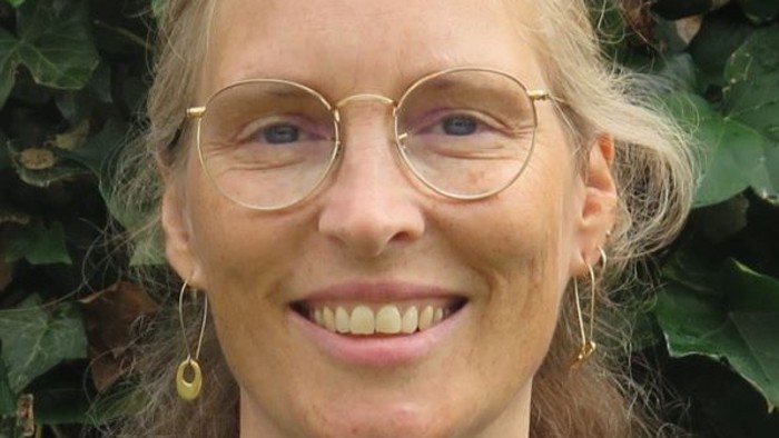 Kvinde med briller og øreringe, der smiler udendørs.