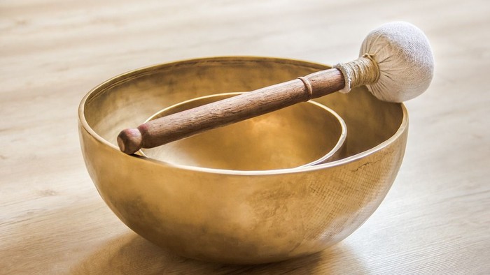 Eine goldene Klangschale mit einem Holzklöppel darin, platziert auf einer Holzfläche.