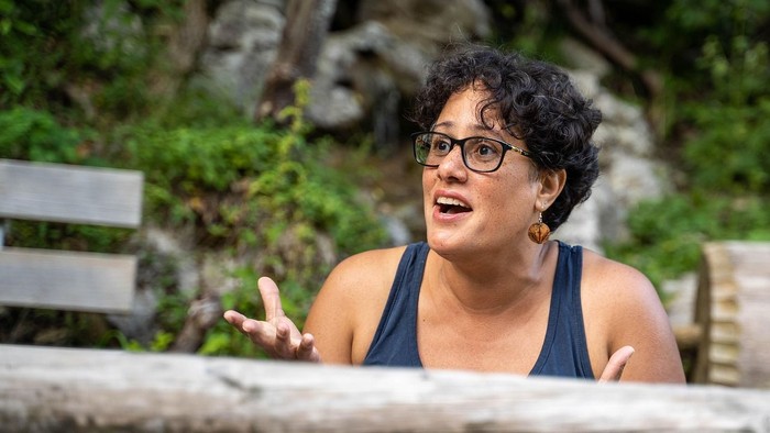 Frau mit Brille, die draußen lebhaft gestikuliert.