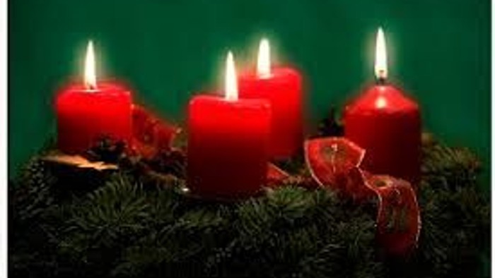 Drei brennende rote Kerzen auf grünem Tannengrün