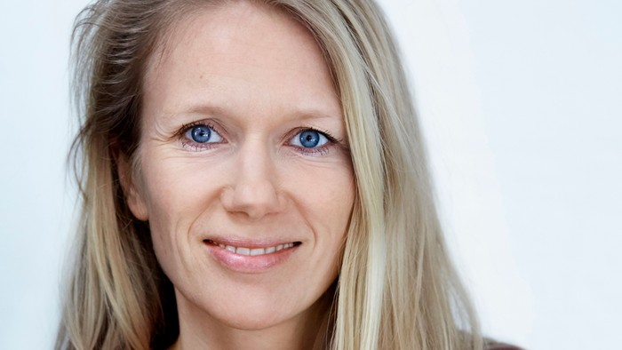 En kvinde med blond hår og blå øjne, smiler til kameraet.