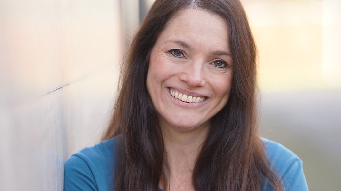 Karen Koers träg hat lange braune Haare, trägt ein blaues Shirt mit längeren Ärmeln und lächelt. Karen Koers ist Pfarrerin der Evangelischen Lydia-Kirchengemeinde in Hagen.