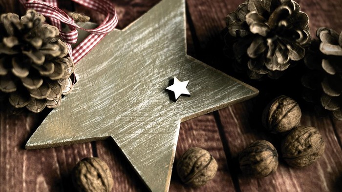 En træstjernepynt omgivet af fyrrekogler og valnødder på en rustik overflade.