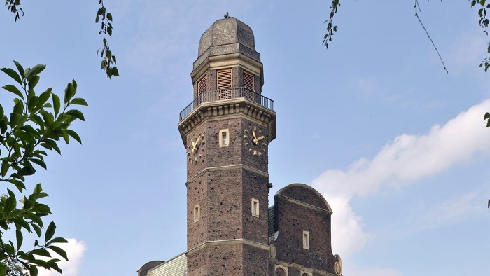 Große Backsteinkirche mit hohem Turm, umgeben von Bäumen und Autos.