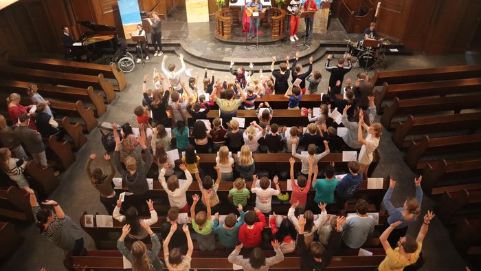 Gottesdienst mit Gemeinde, die die Hände hebt, Chor singt von der Empore.