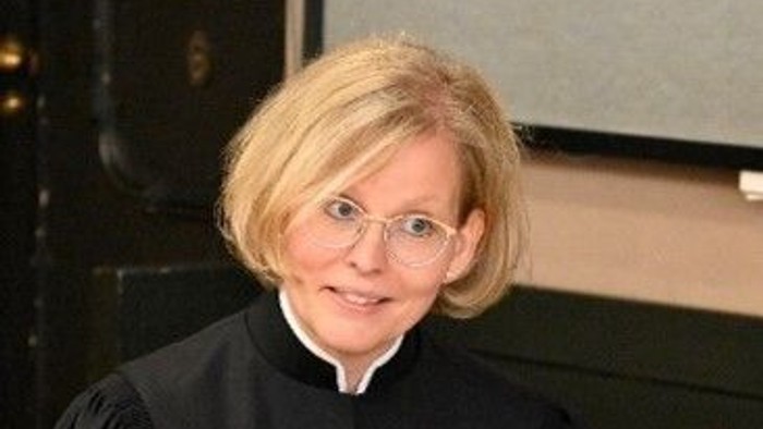 Richter in schwarzer Robe, der Papiere hält und lächelt.