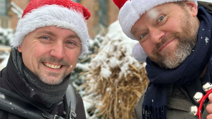 To men i juleskåler og Santa-hatter, en med kamera og den anden med telefon