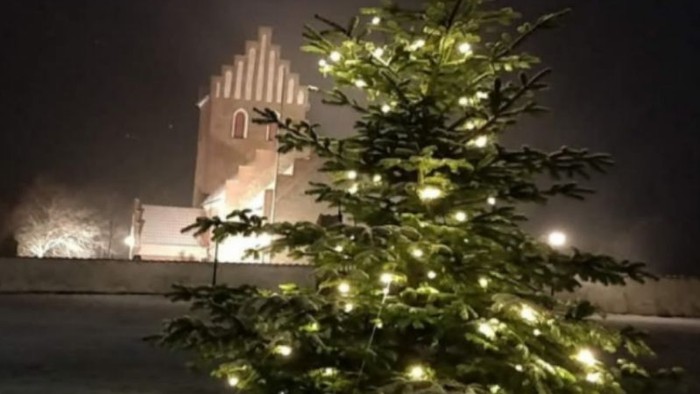 En juletree med lys i forgrunden og et belyset tårn i baggrunden