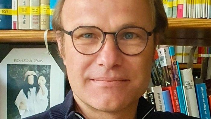 Ein Mann mit Brille und hohem blonden Scheitel vor einem Bücherregal