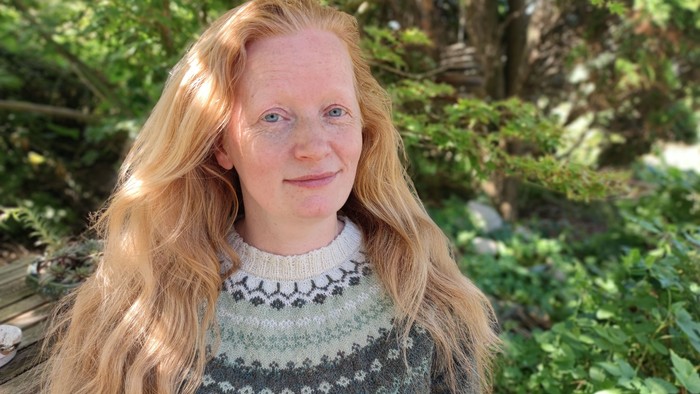 En kvinde med langt blondt hår smiler udendørs.