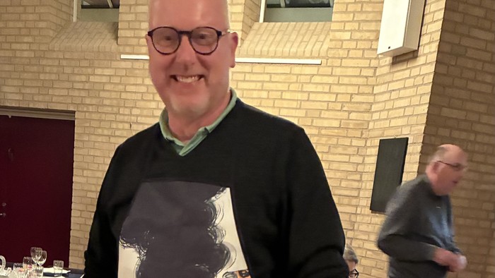 Mand med forklæde med tegnefilmfigurer, der står i et rum med borde og stole.