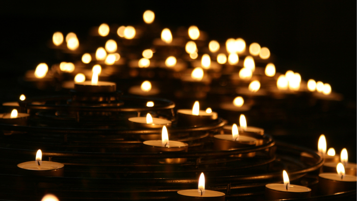 Viele brennende Kerzen, in Reihen angeordnet, mit einer deutschen Botschaft darunter.