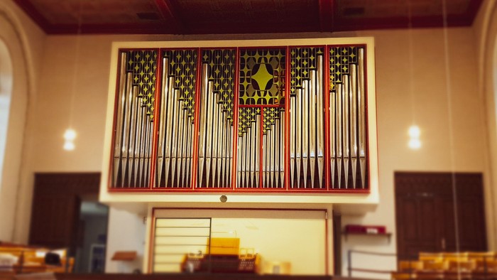 Große Kirchenorgel mit farbenfrohem Fenster im Hintergrund