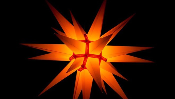 Der leuchtende orangefarbener Hernnhuter Stern vor schwarzem Hintergrund