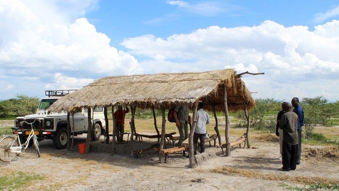 Landrover neben überdachtem Versammlungsort in der Savanne