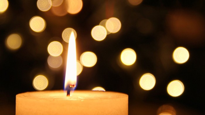 Eine brennende Kerze vor einem unscharfen Hintergrund aus Lichtern