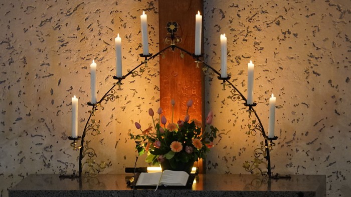 Bild zeigt eine Kirchenbank mit brennenden Kerzen und einem Blumenstrauß