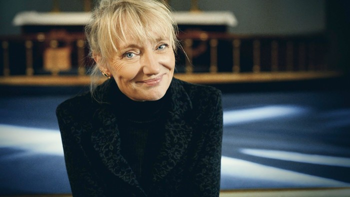 En kvinde med blondt hår og sort trøje smiler i kameraet.