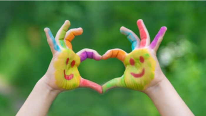 Zwei Hände formen ein Herz mit bunten Handschuhen