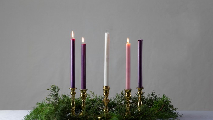 Four lit candles in brass holders on greenery