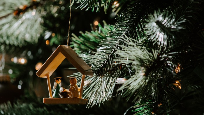 A small wooden birdhouse ornament hangs on a Christmas tree branch.