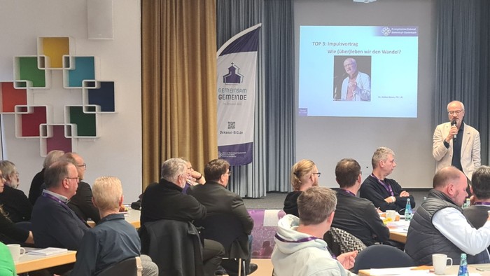 Ein Mann hält auf einer Konferenz einen Vortrag vor einem sitzenden Publikum.