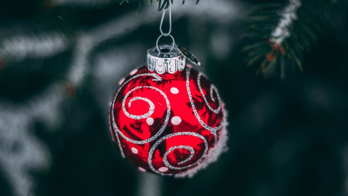 A red Christmas ornament with white swirls hangs from a tree branch.