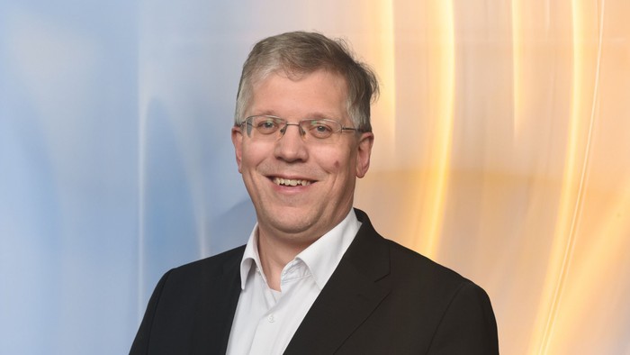 Ein Mann in Anzug und Krawatte lächelt in die Kamera.