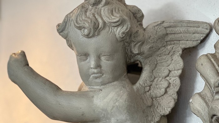 En smuk lille kerubinskulptur med vinger og en arm, der ser ud til at holde noget.