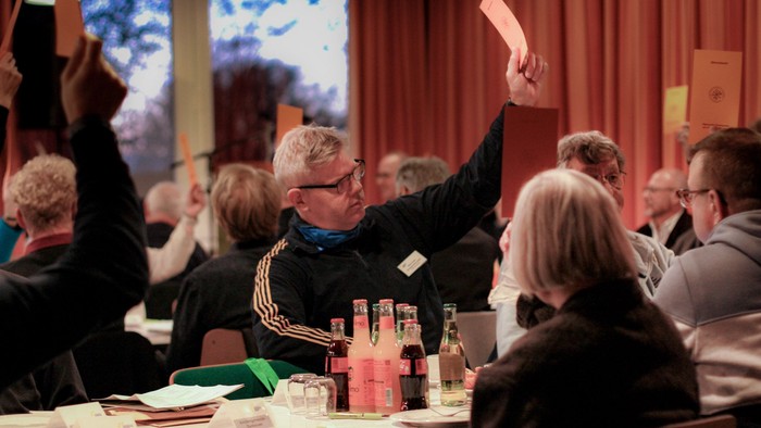 Mehrere Menschen in einem Sitzungssaal heben für eine Abstimmung orange Karten hoch