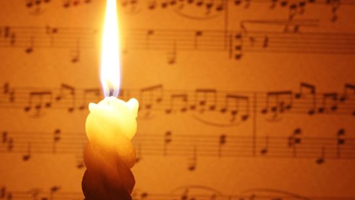 Eine brennende Kerze vor Notenblatt.