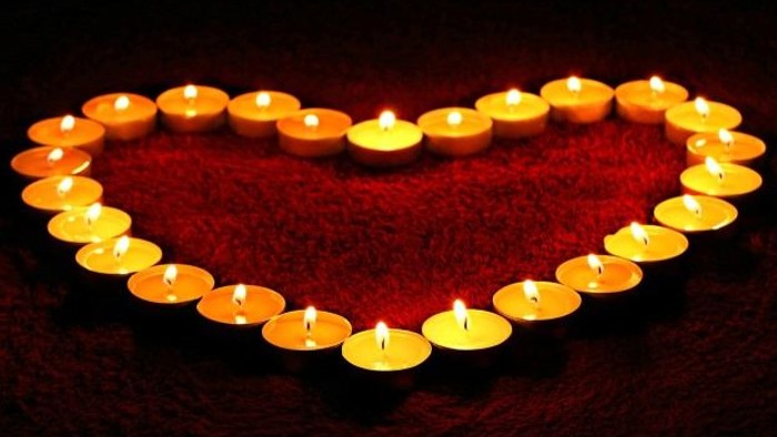 Herzförmige Anordnung von brennenden Kerzen auf rotem Stoff