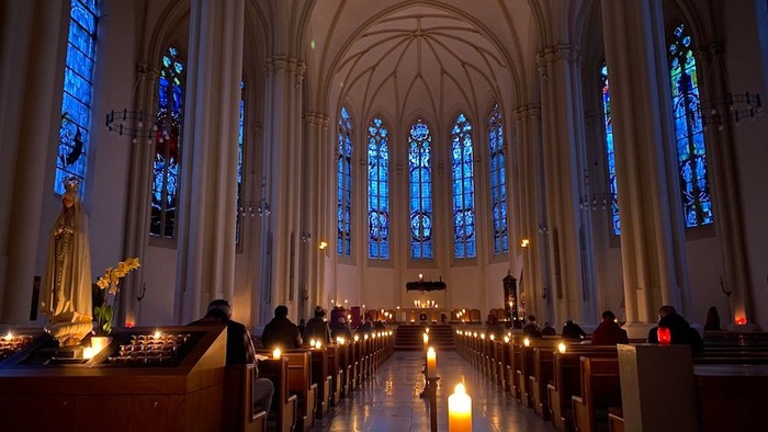 Kircheninneres mit Buntglasfenstern und brennenden Kerzen.