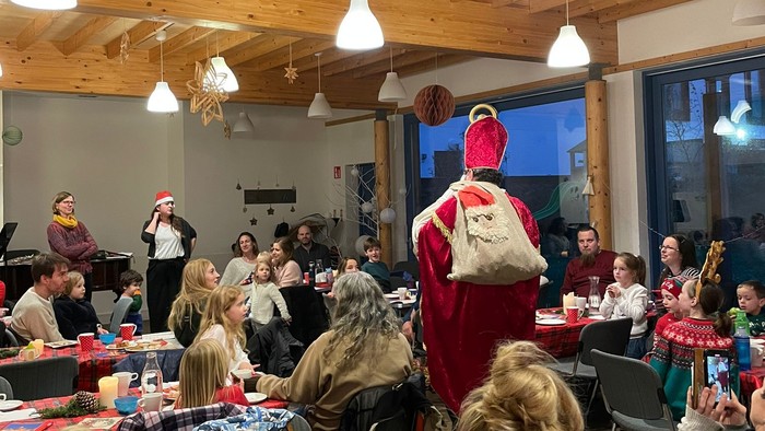 Große Gruppe von Menschen in einem Holzraum, einer in Rot kostümiert steht auf