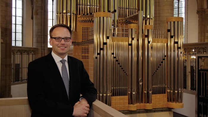 Mann im Anzug steht neben Orgelpfeifen.