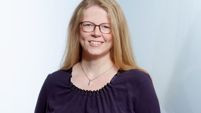 Eine Frau mit blonden Haaren und Brille, die ein lila Oberteil trägt.