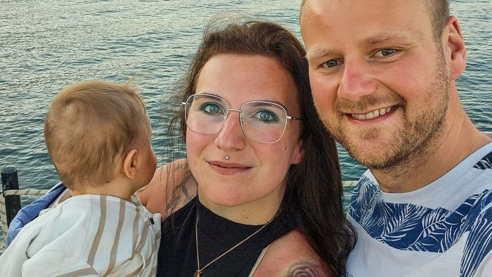 Ein junges Paar hält an einem Ufer ein kleines Kinde auf dem Arm