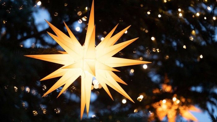 Eine leuchtende sternförmige Deko hängt vor einem dunklen, unscharfen Hintergrund mit Lichtern.