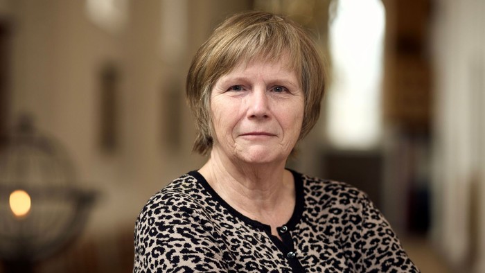 En kvinde med kort hår og leopardmønstrede klæder sidder i et rum med vinduesglas.