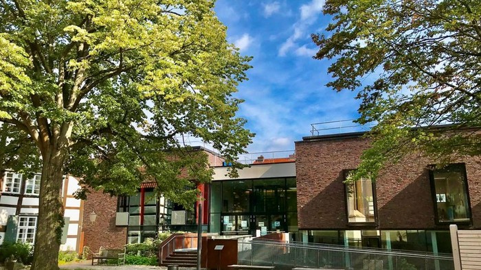 Modernes Gebäude mit Glaseingang, umgeben von Bäumen und klarem blauem Himmel.