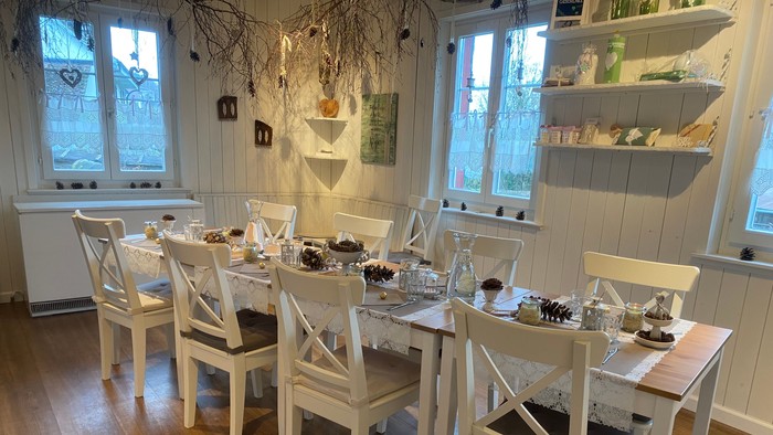 Ein hell eingerichtetes Esszimmer mit mehreren weißen Tischen und Stühlen, die für ein Essen gedeckt sind.