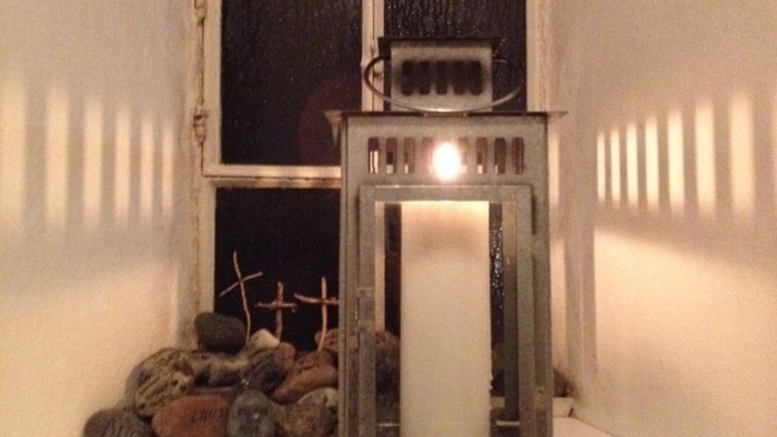 En lysestage med lyset tændt står på et bord med sten og trægrene.