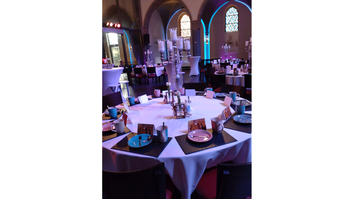 Esstisch in einem Restaurant mit Tellern, Gläsern und Besteck gedeckt, umgeben von bunten Glasfenstern.