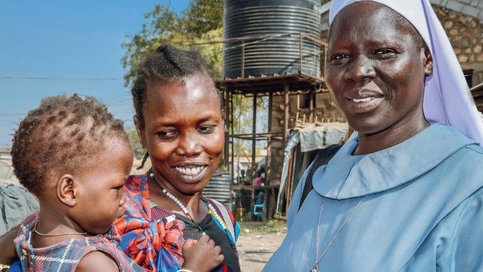 Eine Frau in einem blauen Habit hält ein Baby, während eine andere Frau neben ihr steht, mit deutschem Text und dem „missio“-Logo unten.