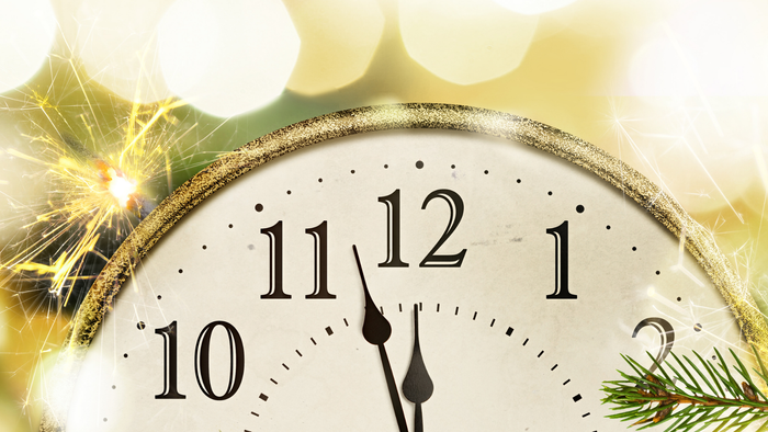 Ein goldener Wecker zeigt die Zeit 12:00, umgeben von Weihnachtsdekorationen.