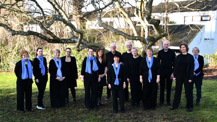 En gruppe mænd i mørke klæder og blå skarves poserer foran et træ og et hus
