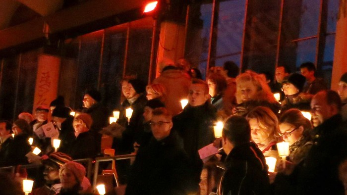 Eine große Gruppe von Menschen hält Kerzen in einem Raum.