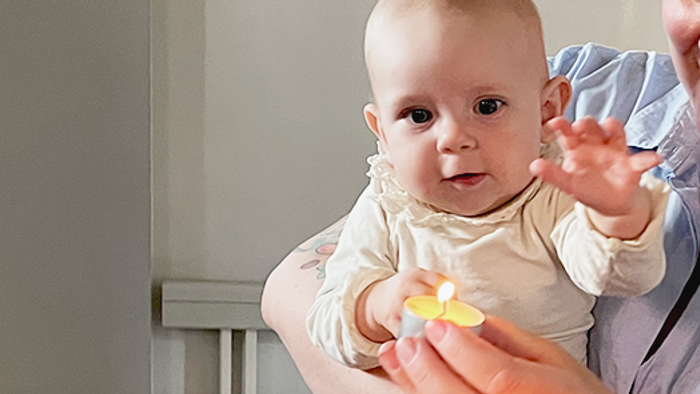 En kvinde holder en baby nær et tændt lys.